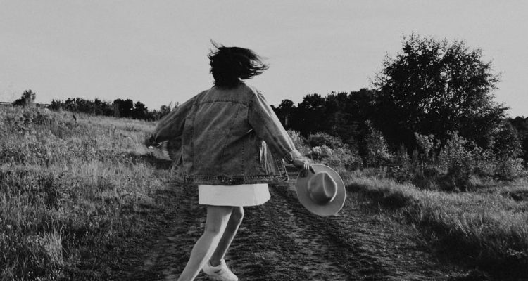 A young girl twirls joyfully outdoors on a sunny day, captured in black and white.